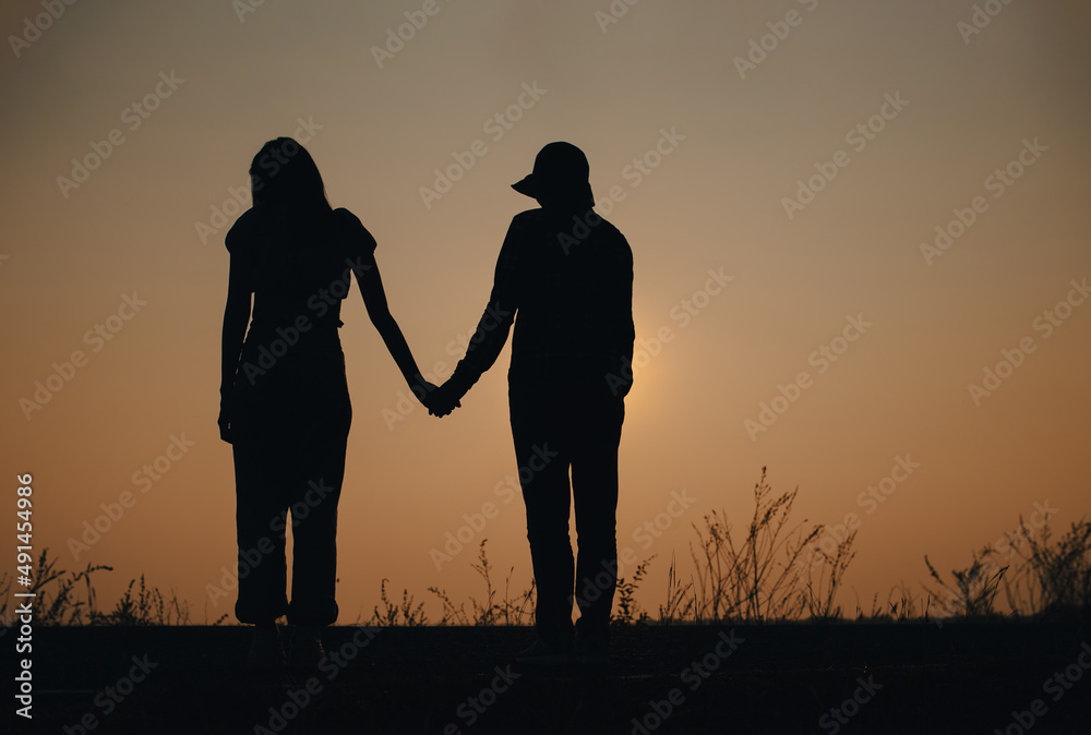 Young couple in love holding hands looking in the sunset