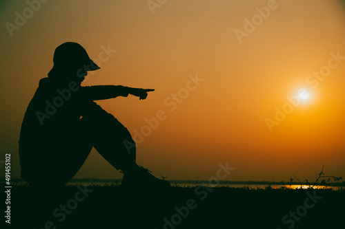 Silhouette of the woman sitting sad at the river during sunset