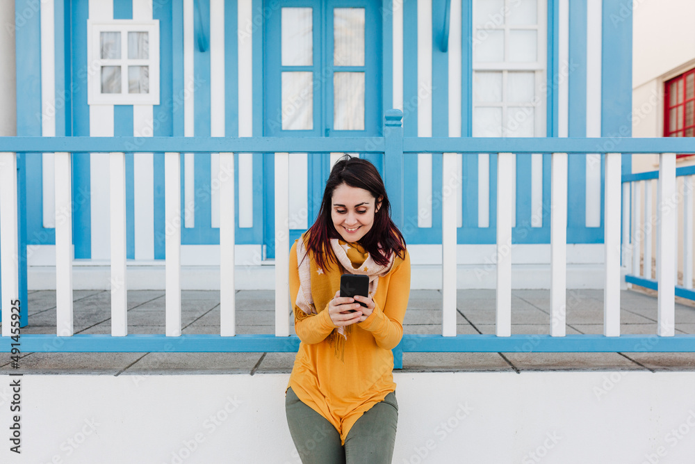 happy woman using mobile phone in front of colorful houses.Costa Nova, Aveiro, Portugal happy woman using mobile phone in front of colorful houses.Costa Nova, Aveiro, Portugal