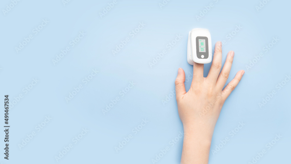 Woman using pulse oximeter finger digital device to measure oxygen  saturation in blood and pulse rate on blue background. Monitor health of  people with pneumonia, anemia or heart failure. Stock Photo