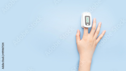 Woman using pulse oximeter finger digital device to measure oxygen saturation in blood and pulse rate on blue background. Monitor health of people with pneumonia, anemia or heart failure. photo