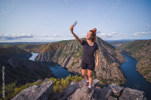 Happy adult woman taking selfie on top of mountain photo