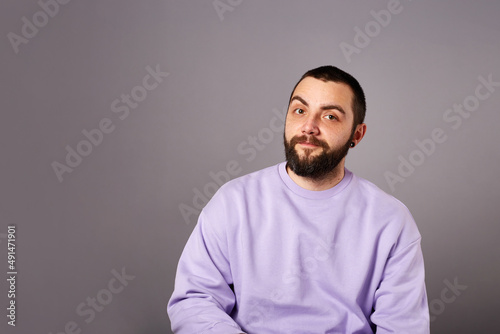 funny bearded man wears violet sweater on grey background. Copy space