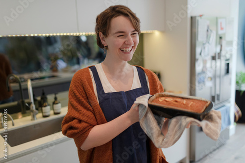 Happy young woman baking loaf cake in kitchen photo