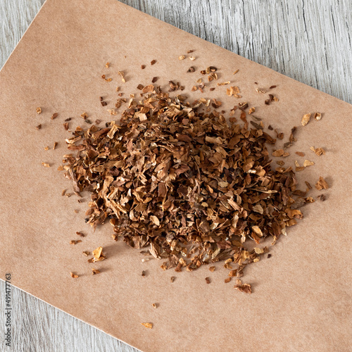 A square photo of dried sliced tobacco or a smoking drug mixture. Smoking drugs on paper close-up on a wooden table. photo