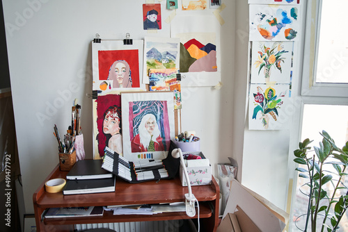 Artist's studio with bright natural light, a lot of creative pictures and artistic tools at the table