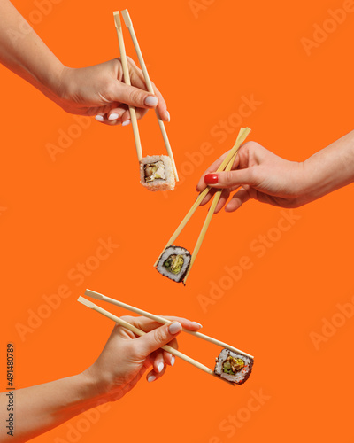 Women's hands hold sushi rolls with sticks. Orange background. Creative concept