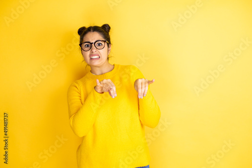 Young beautiful woman wearing casual sweater over isolated yellow background disgusted expression, displeased and fearful doing disgust face because aversion reaction.Annoying concept photo