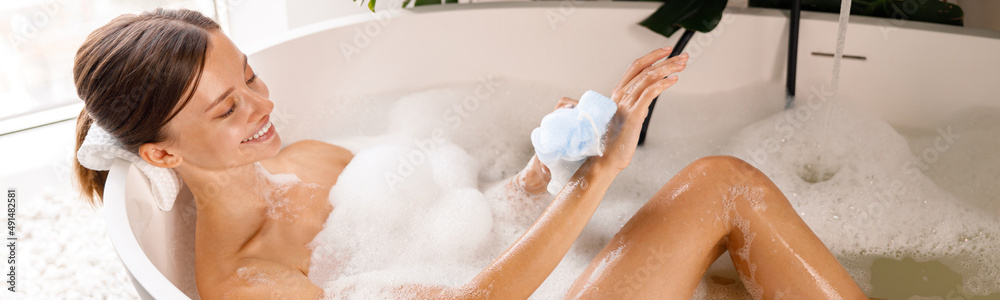 Lovely young woman bathing, using sponge and taking care of her skin, relaxing in the bathtub. Wellness, spa resort concept Lovely young woman bathing, using sponge and taking care of her skin, relaxing in the bathtub. Wellness, spa resort concept