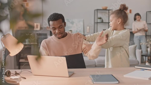 Medium shot of African American 8 year old girl asking her father trying to work on laptop from home to play with her and mans wife calming her down saying not to distract dad from work