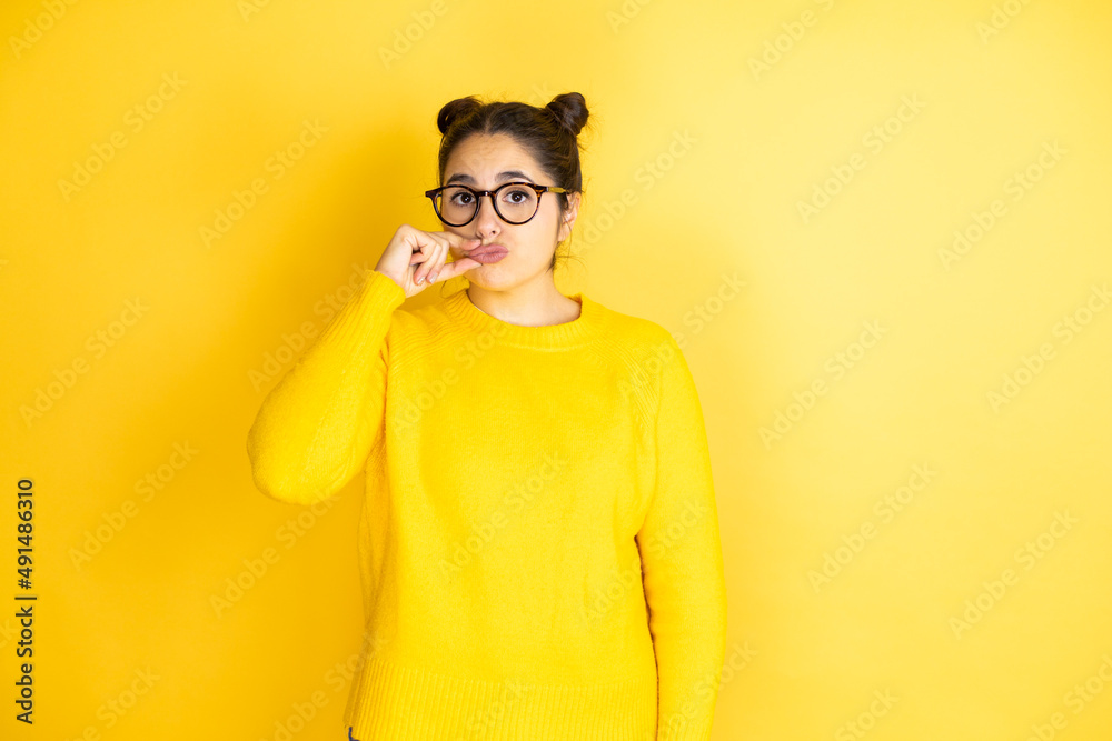 Young beautiful woman wearing casual sweater over isolated yellow background mouth and lips shut as zip with fingers. Secret and silent, taboo talking Young beautiful woman wearing casual sweater over isolated yellow background mouth and lips shut as zip with fingers. Secret and silent, taboo talking