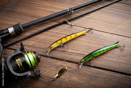 Fishing tackle - fishing spinning rod, hooks and lures on wooden background. Active hobby recreation concept.