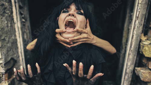 Emotional woman witch in black strangling hands she shouts
