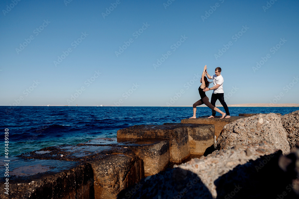 Personal trainer man correct woman client while doing stretching or yoga outdoors background sea. Concept asana instructor support