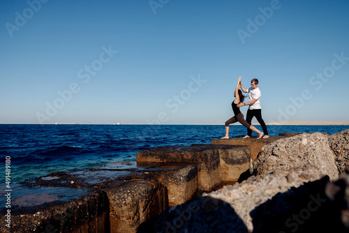 Personal trainer man correct woman client while doing stretching or yoga outdoors background sea. Concept asana instructor support