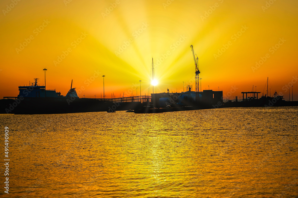 Stunning backlit landscape of sunset golden hour with sunbeams in the sea port