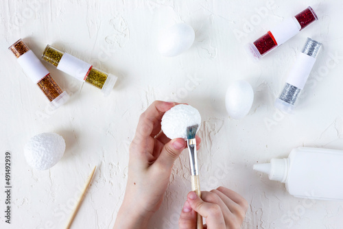 child's hands apply glue to a styrofoam egg, decorating styrofoam eggs with glitter for a festive easter table. step1 photo