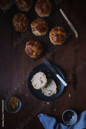 Flat lay Easter theme food image shot from above. Freshly baked and served on a plate hot cross buns. Ingredients and baking utensils in shot. Copy space available. Dark and vintage style