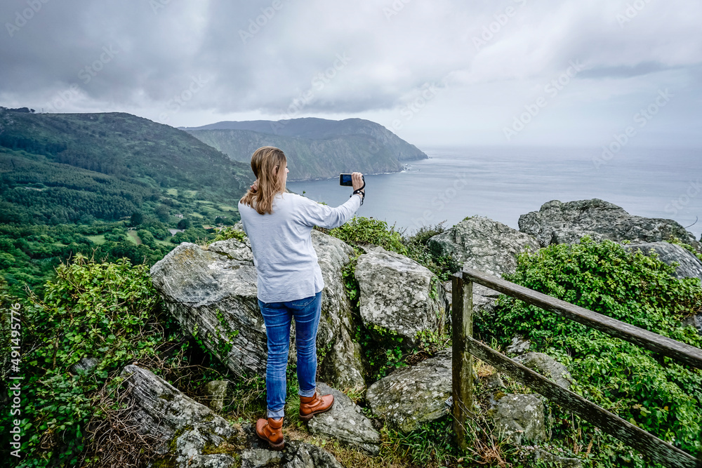 Naklejka premium Young and beautiful woman taking photos with the mobile on the coast of Galicia