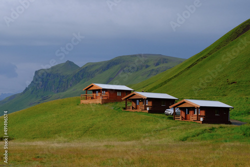 3 wooden country houses (cottage village) stand next to the mountain on the background of mountains covered with green grass in Iceland. Landscape with tourist houses (hotels) in Iceland