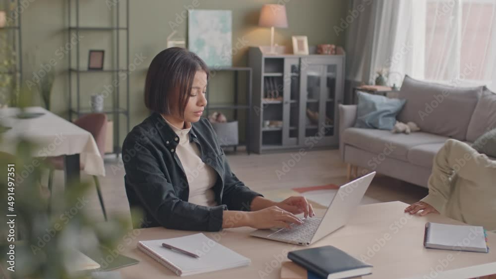 Medium slowmo of playful 8 year old African American girl distracting her busy mother from work on laptop from home Medium slowmo of playful 8 year old African American girl distracting her busy mother from work on laptop from home