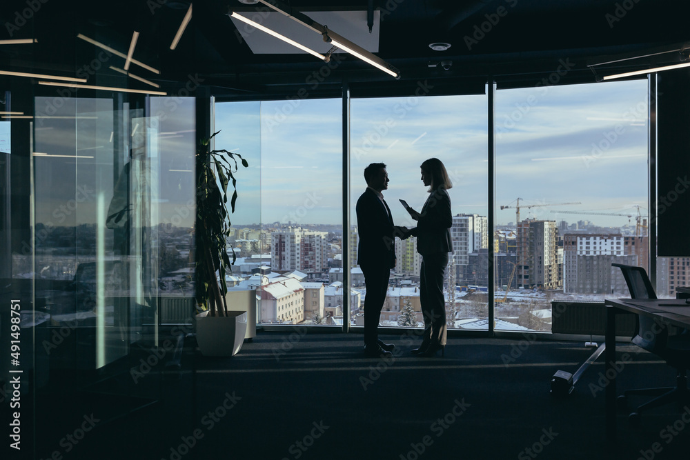 Silhouettes of two employees team of businessmen, Asian man and woman are consulting and communicating, working in a modern office by the window Silhouettes of two employees team of businessmen, Asian man and woman are consulting and communicating, working in a modern office by the window