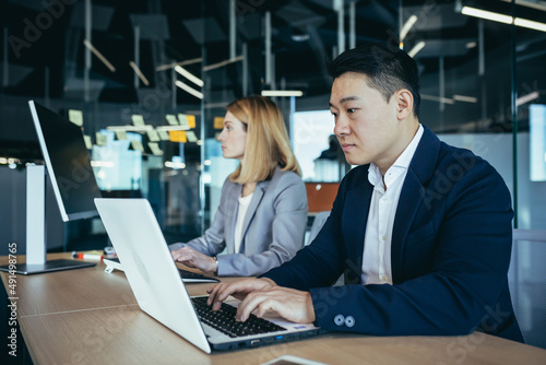 Asian businessman working in modern office on laptop, happy and successful, team of employees, man and business woman, startup