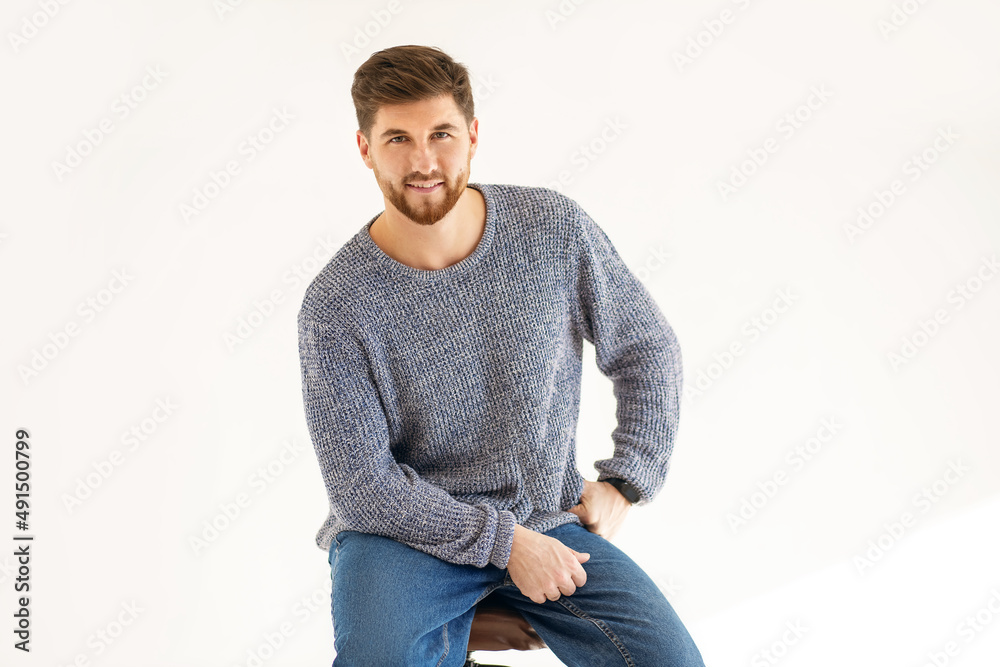 Handsome man with a beard dressed in casual clothes on a white background. A man with a stylish hairstyle and beard sits on a chair and smiles. Portrait of a confident male dressed in jeans Handsome man with a beard dressed in casual clothes on a white background. A man with a stylish hairstyle and beard sits on a chair and smiles. Portrait of a confident male dressed in jeans