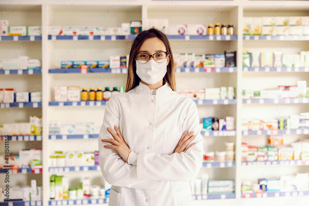 A successful young female pharmacist at pharmacy with arms crossed ready to help.