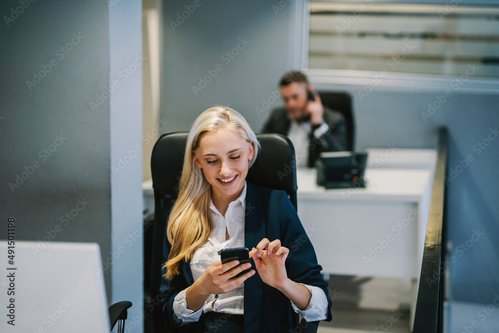 A businesswoman sitting at workstation and smiling at the phone. A businesswoman sitting at workstation and smiling at the phone.