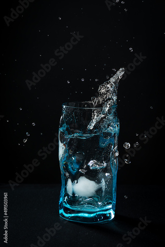 Ice falls into the glass. splash of frozen water. Blue beautiful wine glass