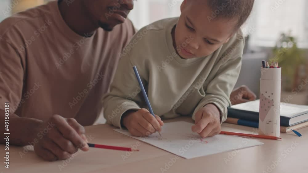 Medium closeup with slowmo of little African American girl and her dad sitting at desk in living room drawing pictures Medium closeup with slowmo of little African American girl and her dad sitting at desk in living room drawing pictures