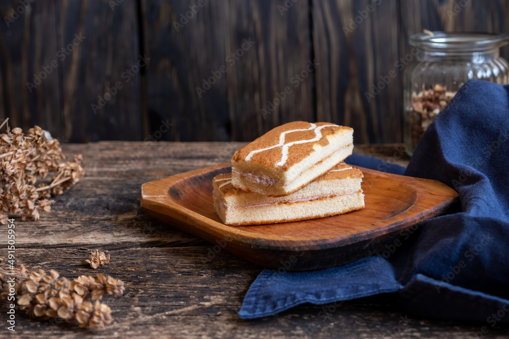 Square shaped mini cakes on a wooden surface, dark blue material, dried basil and a jar of nuts Square shaped mini cakes on a wooden surface, dark blue material, dried basil and a jar of nuts