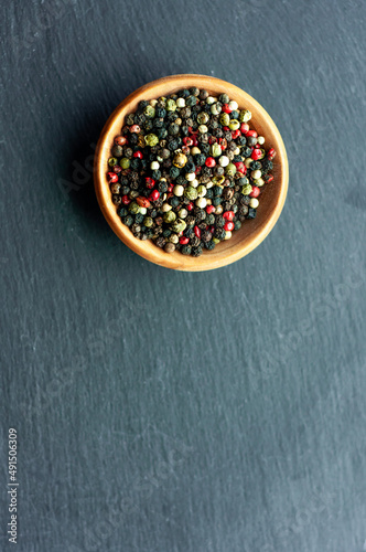 peppercorns, black pepper, white, green, red pepper, aromatic seasoning, spices, cooking ingredients, top view, in a wooden bowl on a black background, space for text 