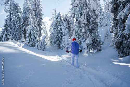Footage of the back of a young hiker with a white ski costume and a bright colorful hat walking in the snow