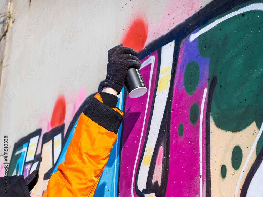 Fototapeta premium street artist draws colorful and vibrant graffiti. Modern art concept with city guy, artist applies bright graffiti on gray wall