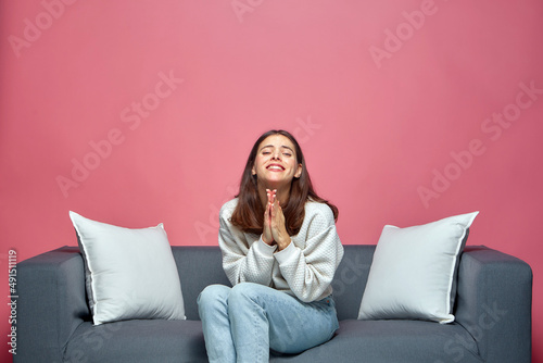 Young girl folded hands begging, asking help, support, apologizing, sitting on sofa, praying for heroes of series