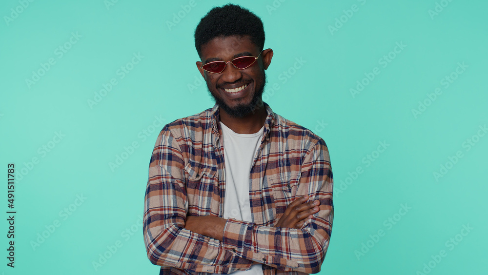 Fototapeta premium Portrait of seductive cheerful casual african american man wearing red sunglasses, charming smile. People emotions concept. Young lovely adult guy posing isolated alone on blue studio wall background