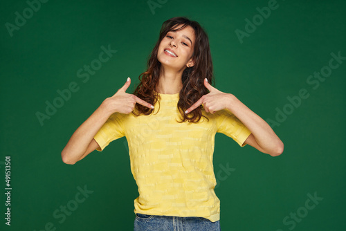 I am best. Smiling young girl pointing by fingers on herself, proud of her success on green studio background. Choose me © Georgii