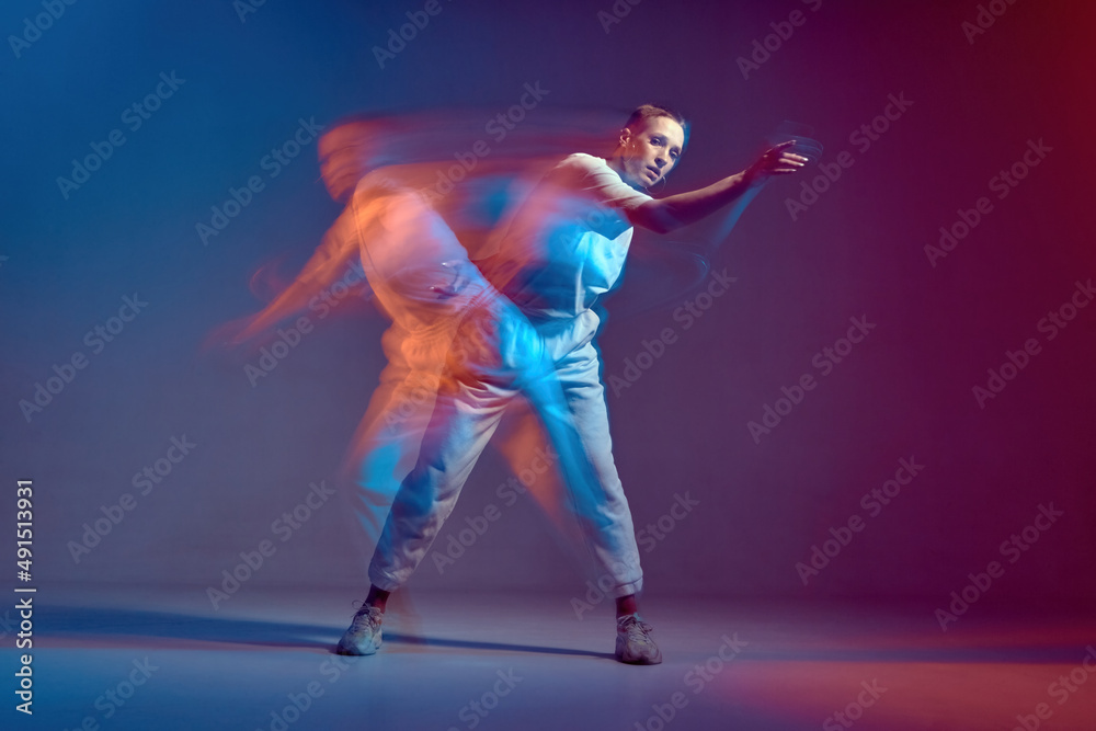 Young stylish girl in action, motion, dancing hip-hop. Breakdancer in colourful neon light at dance hall. Long exposure