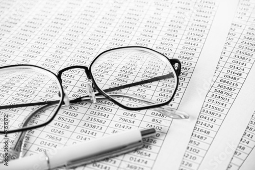 Elegant white pen on a pile of paper documents with blurred glasses is background. Business concept. Report  pay tax  finance.