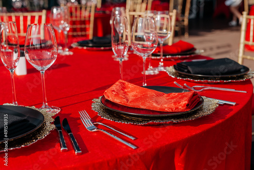 Guests table setting for banquet in black, red and gold style. Elegant and luxury dinner arrangement: decor, tablecloth, plates, glasses, napkins, cutlery. Themed birthday or wedding party celebration