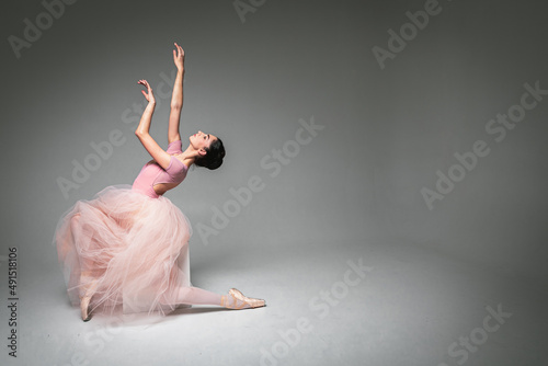 Fototapeta young pretty, fragile, beautiful ballerina dancing in a long pale pink dress with a tulle on a uniform background, hand movements, restrained tone