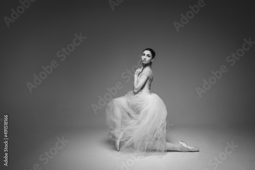 black-and-white photo, young pretty, fragile, beautiful ballerina dancing in a long pale pink dress with tulle on a uniform background, hand movements, restrained tone. Ballet, dance, dancer. Place fo