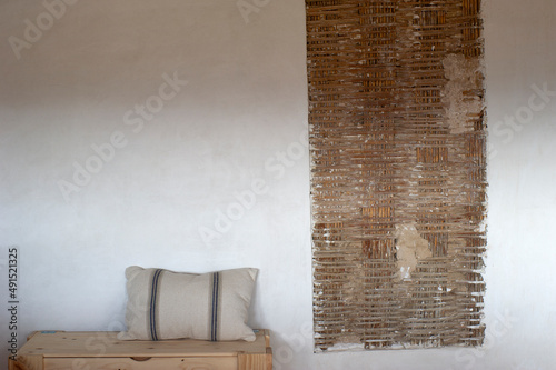 Banco madera con almohada, pared blanca con trozo con cañizo photo