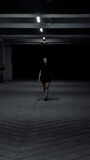 woman walking in parking lot at night with light dressed in black