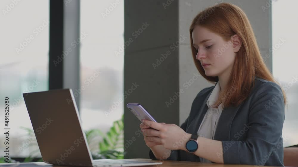 Beautiful young business woman using phone in office. Woman using a smartphone and leaning on a window texting sending emails planning meetings networking online browsing messages on mobile phone Beautiful young business woman using phone in office. Woman using a smartphone and leaning on a window texting sending emails planning meetings networking online browsing messages on mobile phone