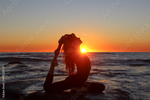 silhouette of a young woman doing yoga on the beach at sunset