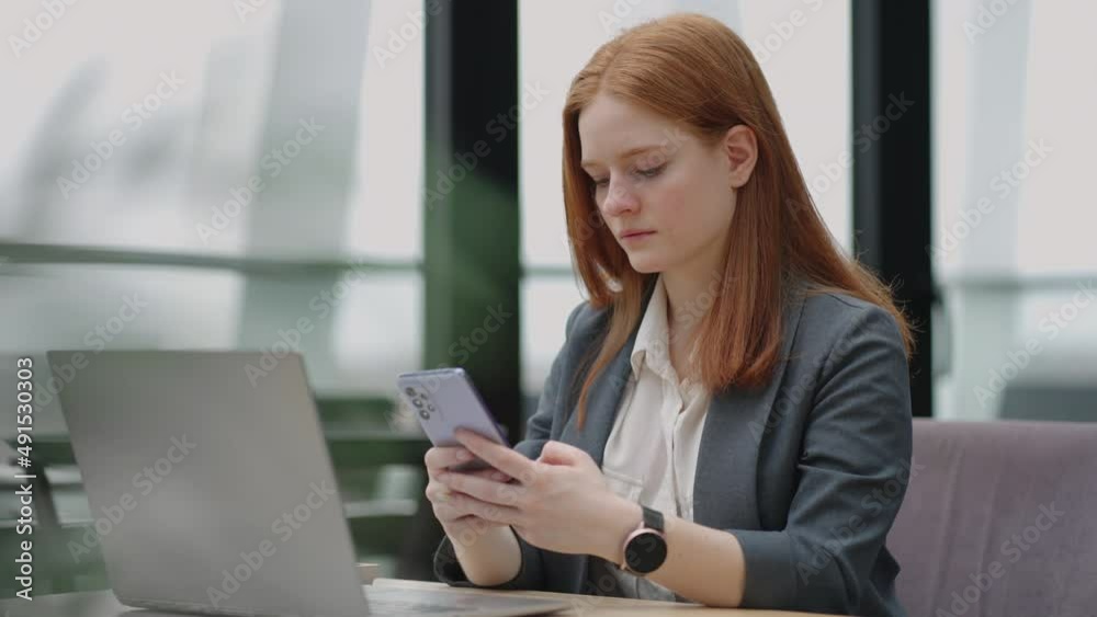 Beautiful young business woman using phone in office. Woman using a smartphone and leaning on a window texting sending emails planning meetings networking online browsing messages on mobile phone Beautiful young business woman using phone in office. Woman using a smartphone and leaning on a window texting sending emails planning meetings networking online browsing messages on mobile phone