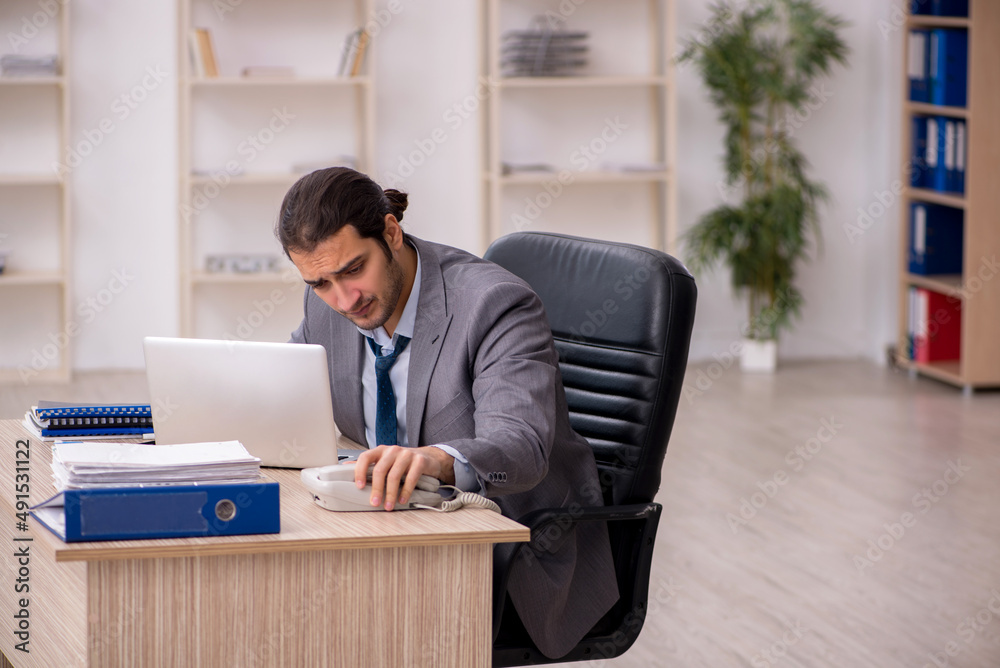 Young male employee unhappy with excessive work in the office Young male employee unhappy with excessive work in the office